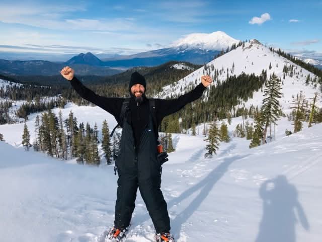 DamiEl Balderrama celebrating on a snowy ridge near Heart Lake with Mount Shasta in the background