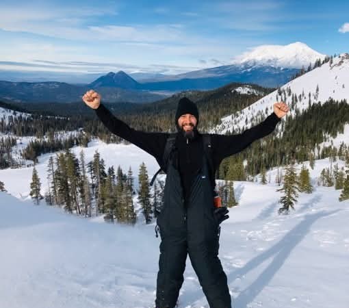 DamiEl Balderrama celebrating on a snowy ridge near Heart Lake with Mount Shasta in the background